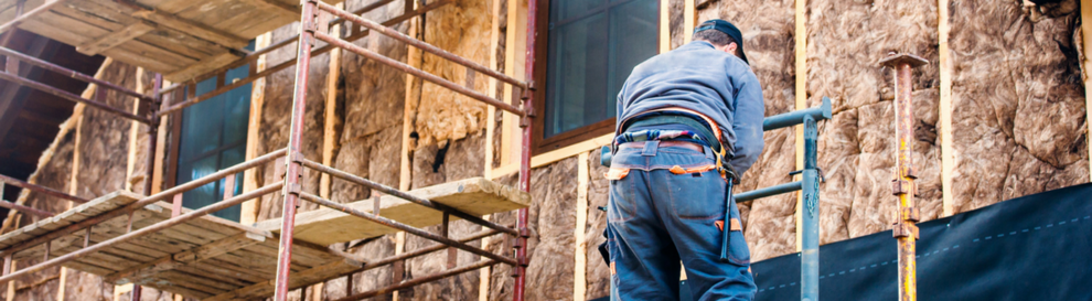 Handwerker auf dem Baugerüst vor einer gedämmten Fassade.